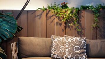 A wooden fence with climbing plants and flowers, a sofa with patterned cushions, and a hanging light fixture.