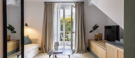 Une pièce confortable avec un canapé, une petite table agrémentée d’un objet décoratif, un téléviseur et une vue sur la verdure à l’extérieur.