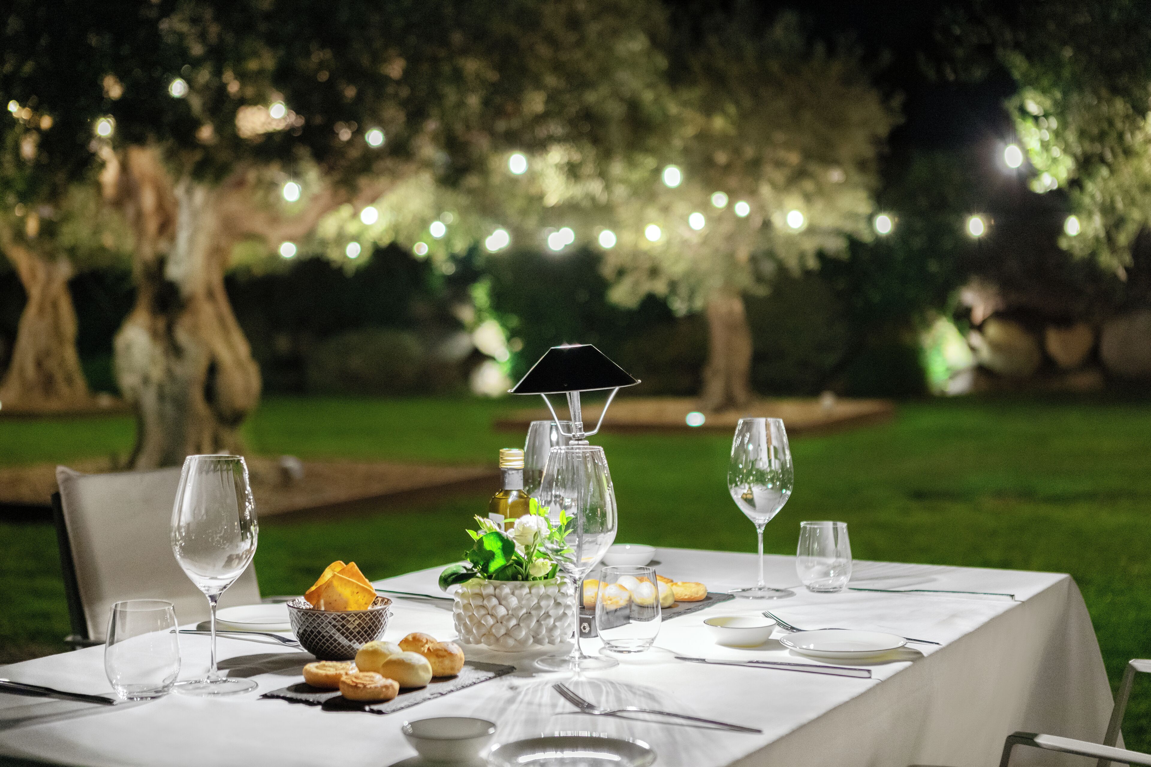 Mesa de comedor exterior con copas de vino, platos y un centro de mesa.