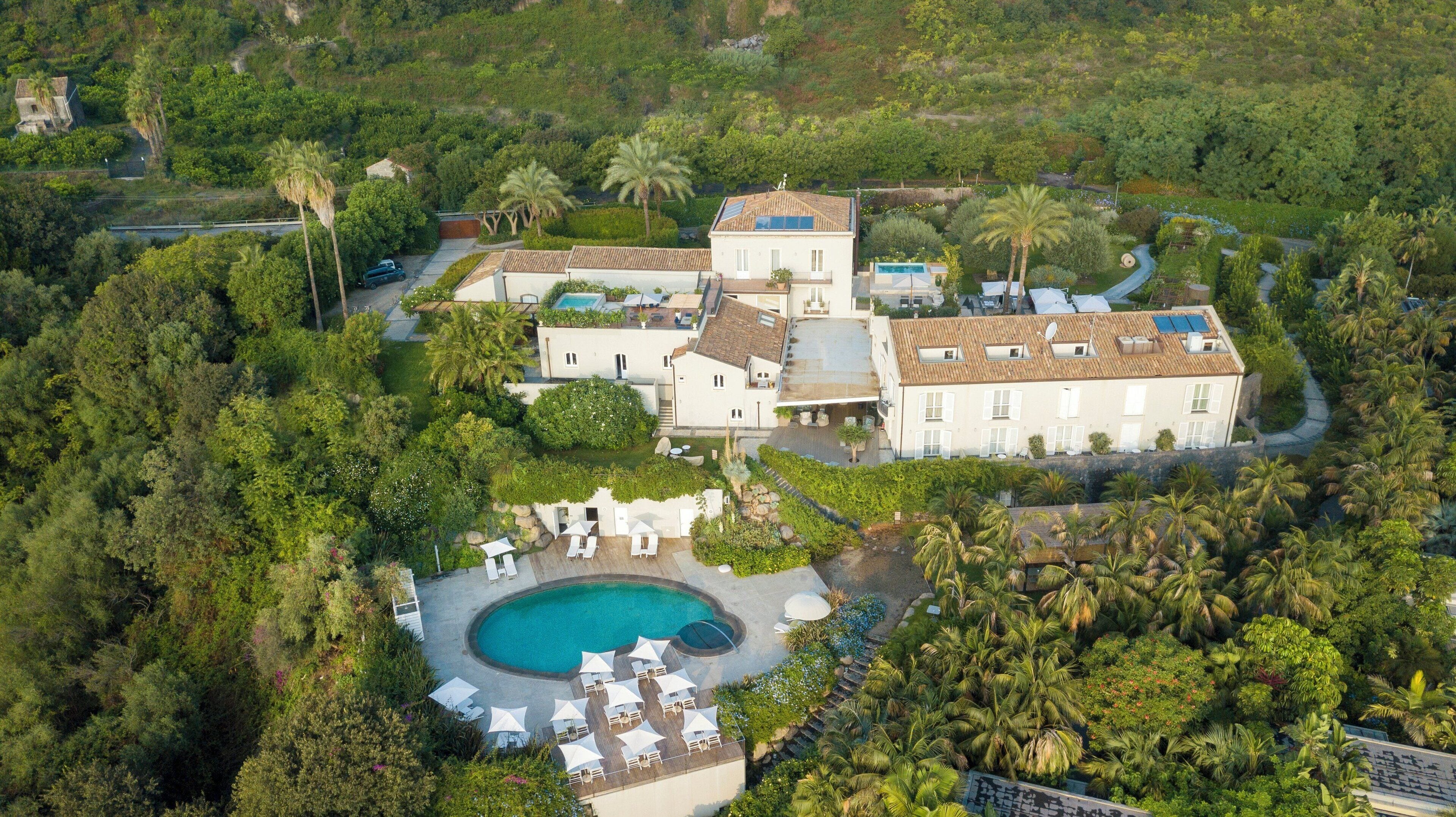An aerial view of a large, multi-story property with a swimming pool, multiple buildings, and lush greenery.