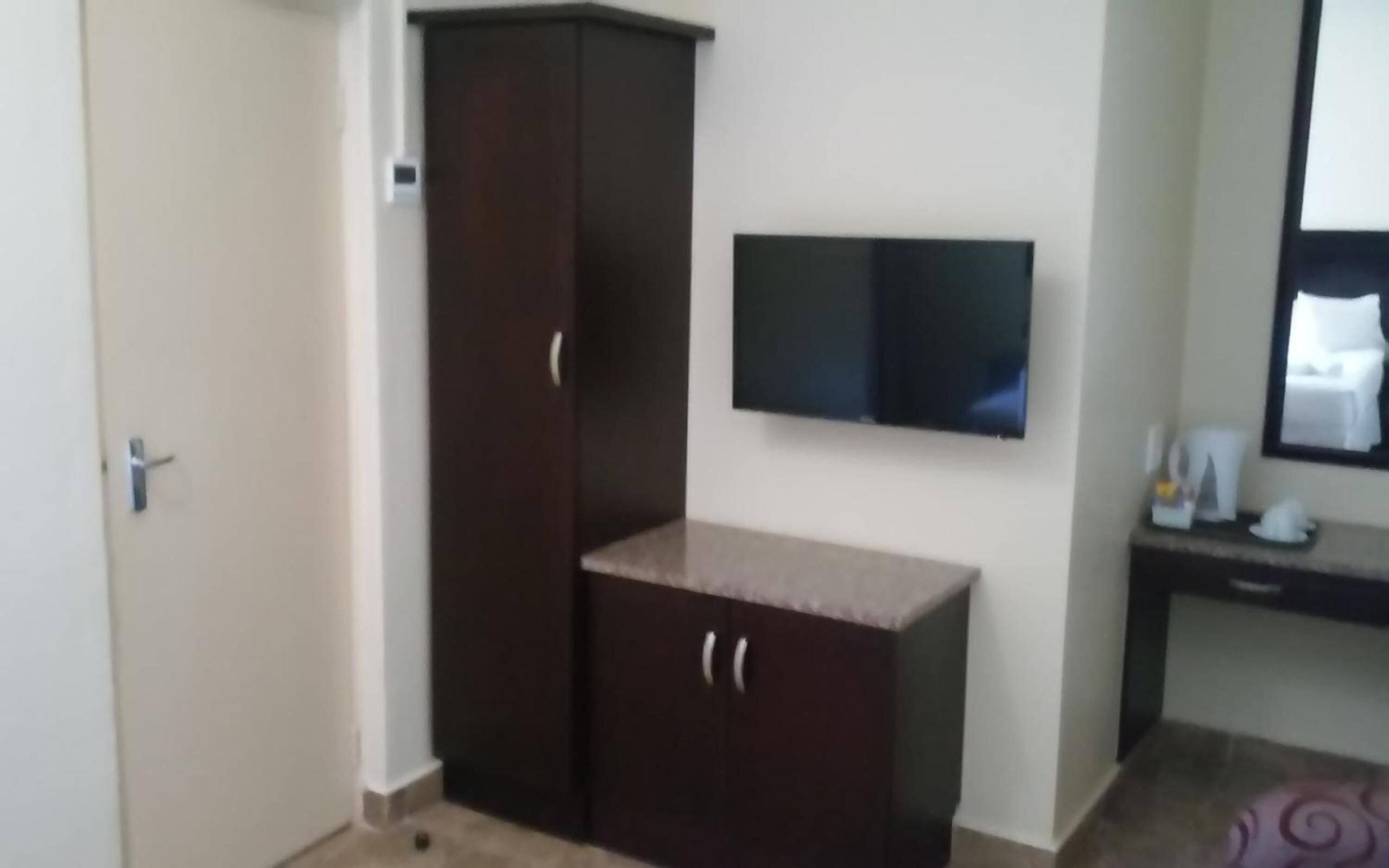 Een kamer met een garderobe, een wandgemonteerde flatscreen-tv en een klein tafeltje met een spiegel en enkele spullen erop.