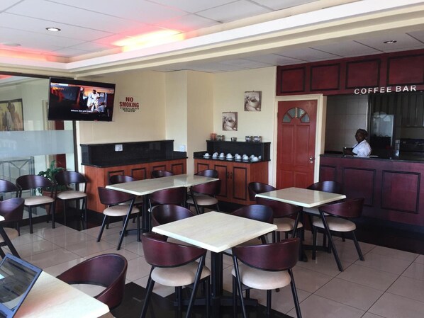 Un área de cafetería con mesas y sillas, una pantalla de televisión y un letrero que dice 'NO SMOKING'.