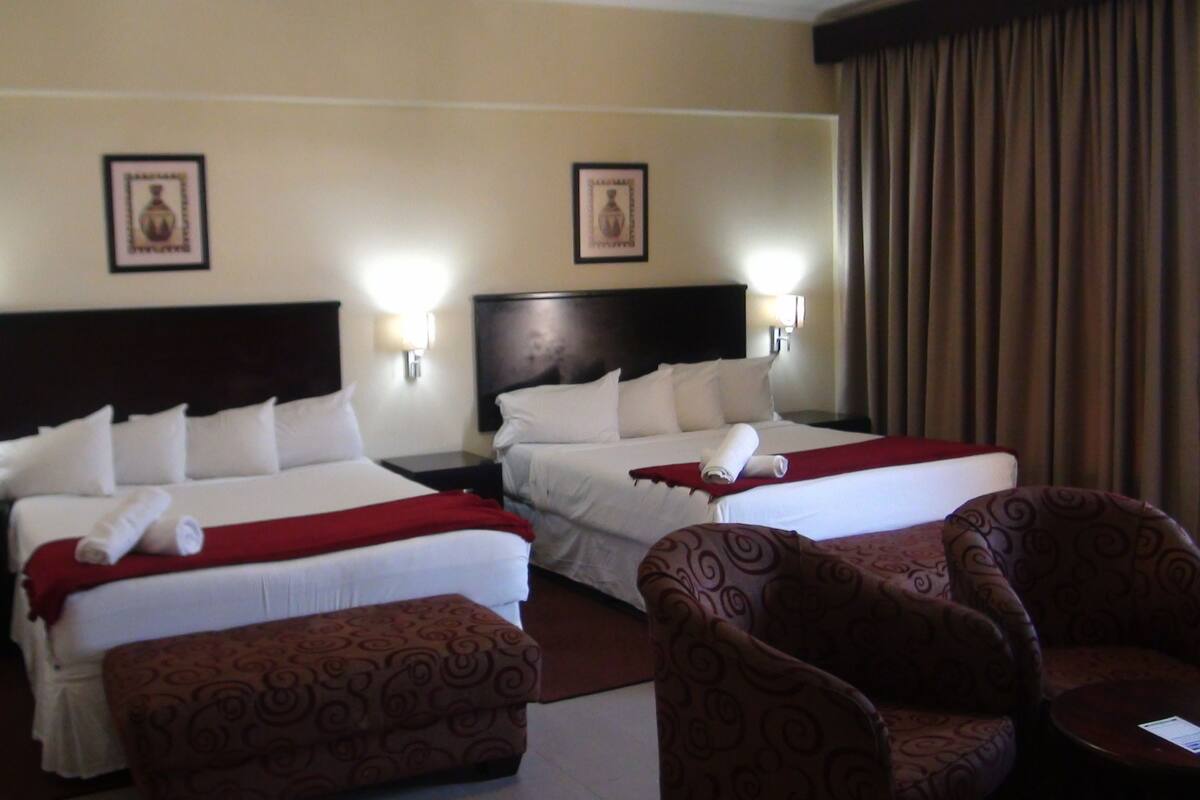 Una habitación de hotel con dos camas, un reposapiés rojo y sillones a juego.