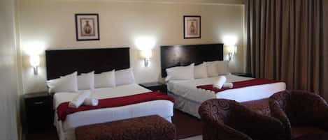 Una habitación de hotel con dos camas, un reposapiés rojo y sillones a juego.