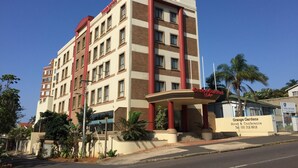 Un hotel de varios pisos con una fachada destacada en rojo y beige, que presenta una entrada amplia con escalones y un letrero.
