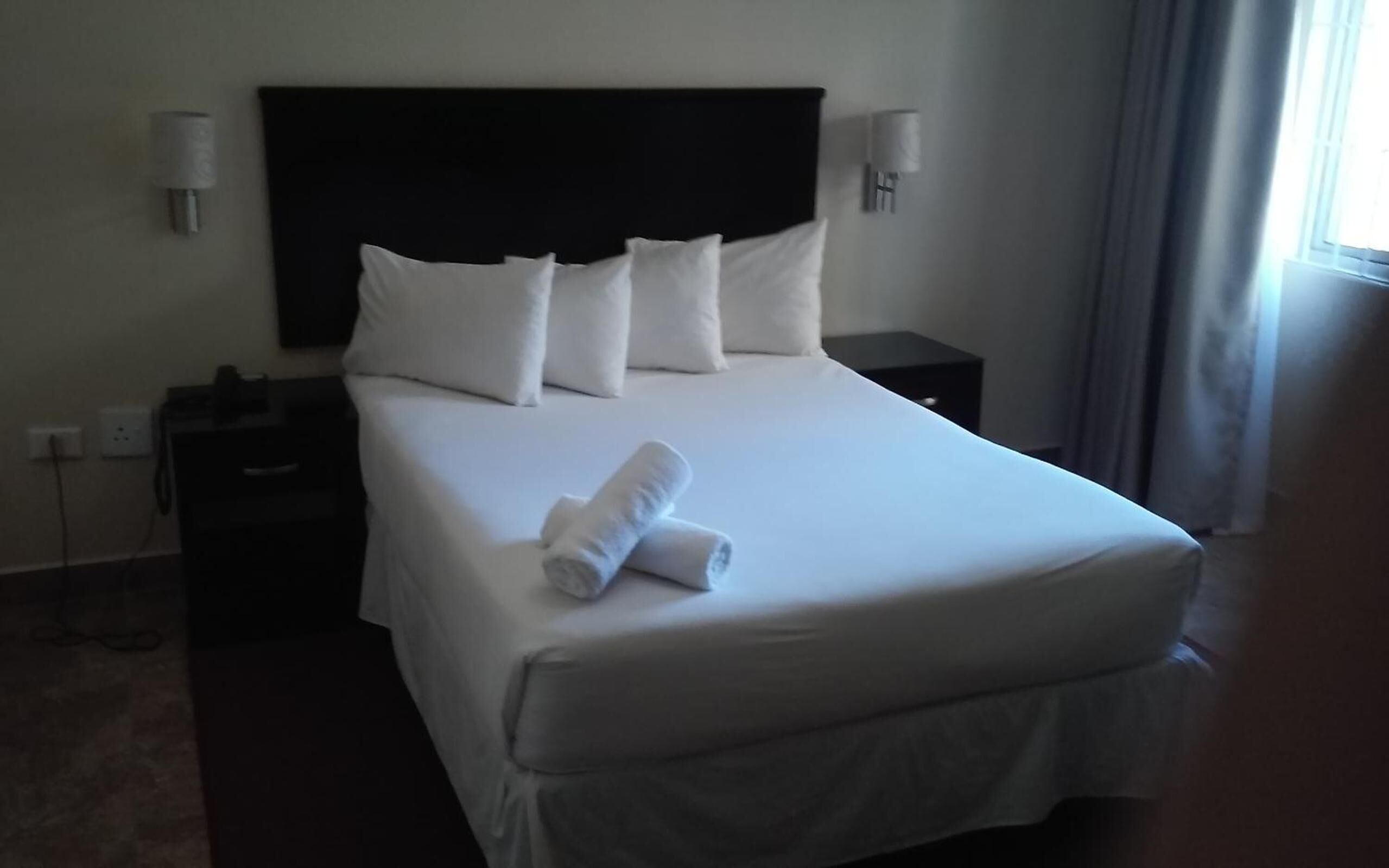 Quarto de hotel com uma cama grande, duas mesas de cabeceira e um criado-mudo.