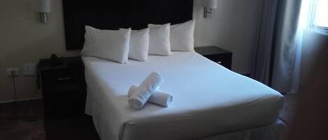 Quarto de hotel com uma cama grande, duas mesas de cabeceira e um criado-mudo.