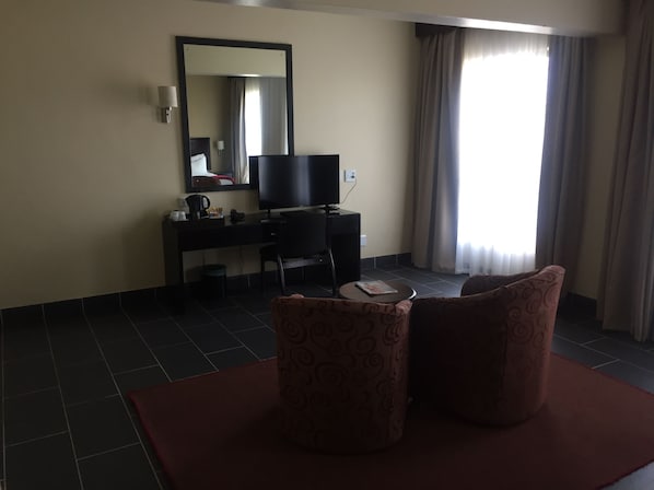 Habitación de hotel con escritorio, silla, televisor, espejo y ventana con cortinas.