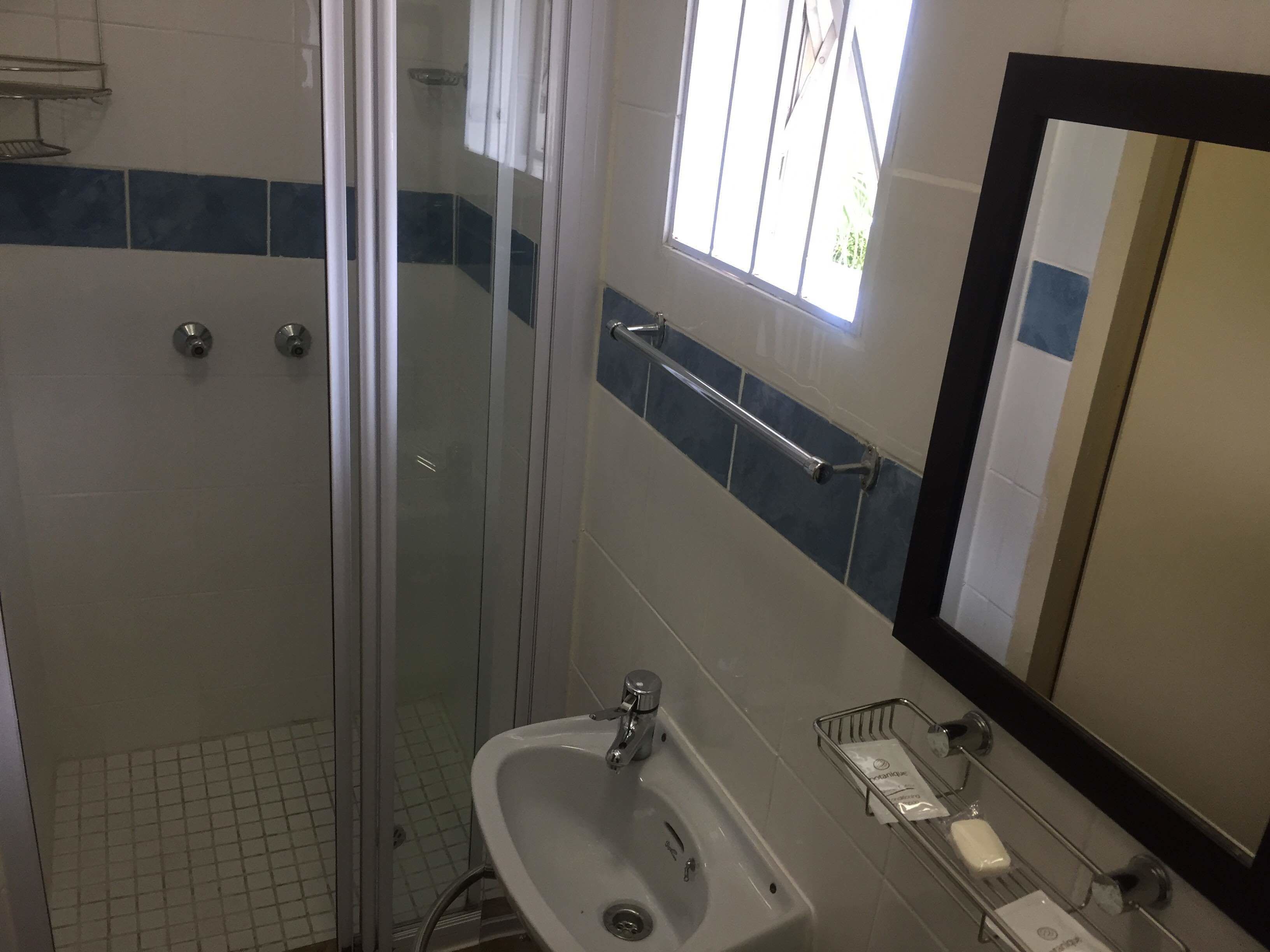 A bathroom with a glass shower enclosure, a sink with a mirror, and a window providing natural light.