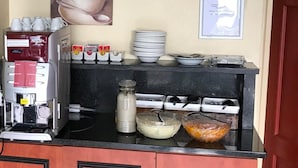 Una kitchenette con cafetera, tazas y dispensador de leche.