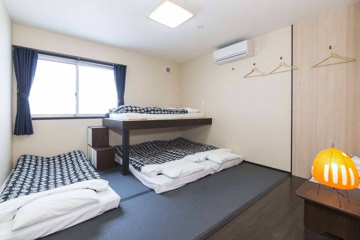 A compact room with bunk beds, a window with curtains, an air conditioning unit, and a small table with a lamp.