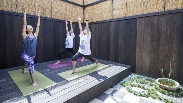 Una terraza de madera con tres personas practicando yoga.