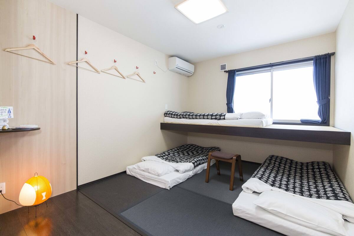 A compact hotel room with a bunk bed, a small desk, a chair, and a window with curtains.