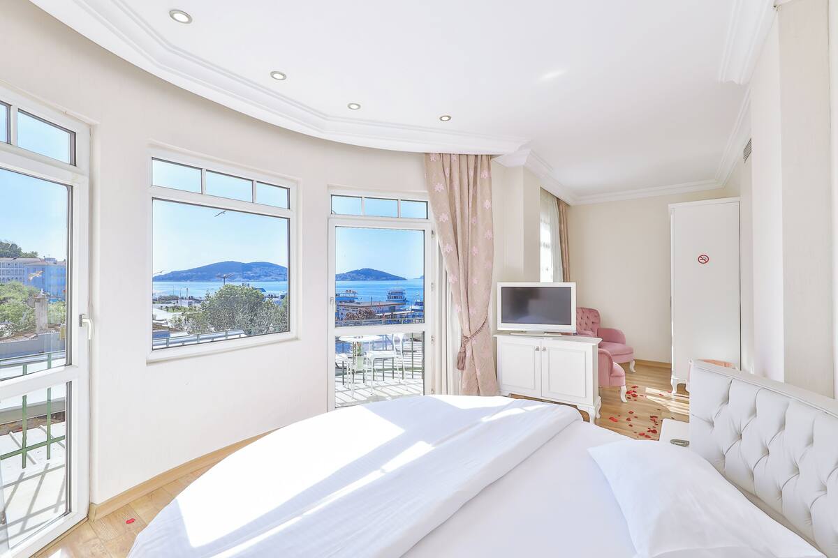 Une chambre à coucher comprenant un lit, une télévision, une armoire et un balcon avec vue sur la mer et les montagnes.