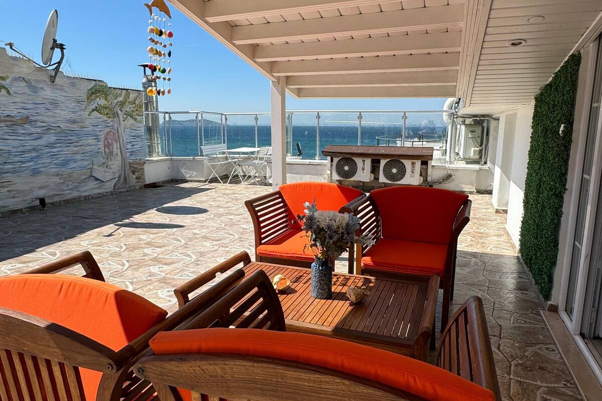 Une terrasse extérieure avec des meubles en bois, une table agrémentée d’un vase et une vue sur la mer.