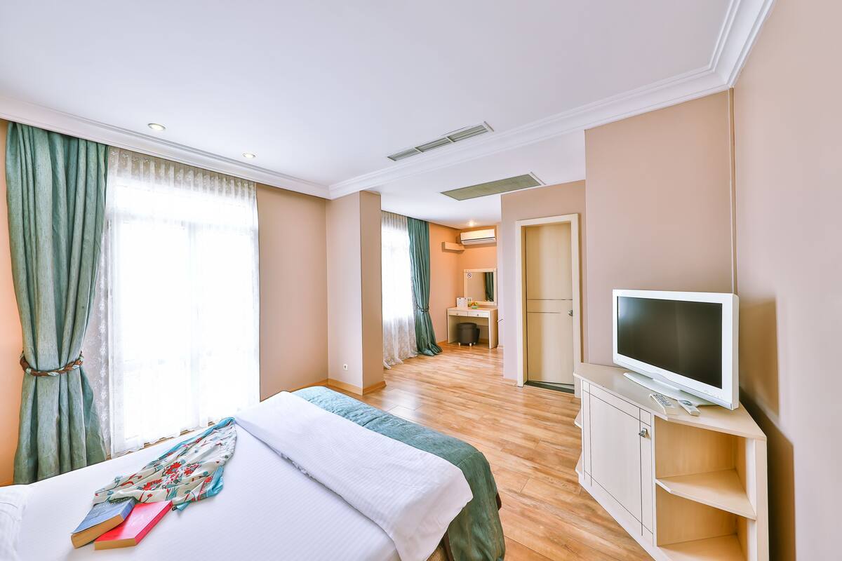 Une chambre d’hôtel avec un lit, un téléviseur posé sur un meuble, un bureau et une salle de bain visible à travers une porte ouverte.