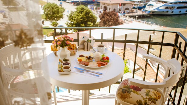 A balcony with a table set for breakfast, overlooking a marina with boats and a coastal view. - Buyukada Princess Hotel (Adalar)