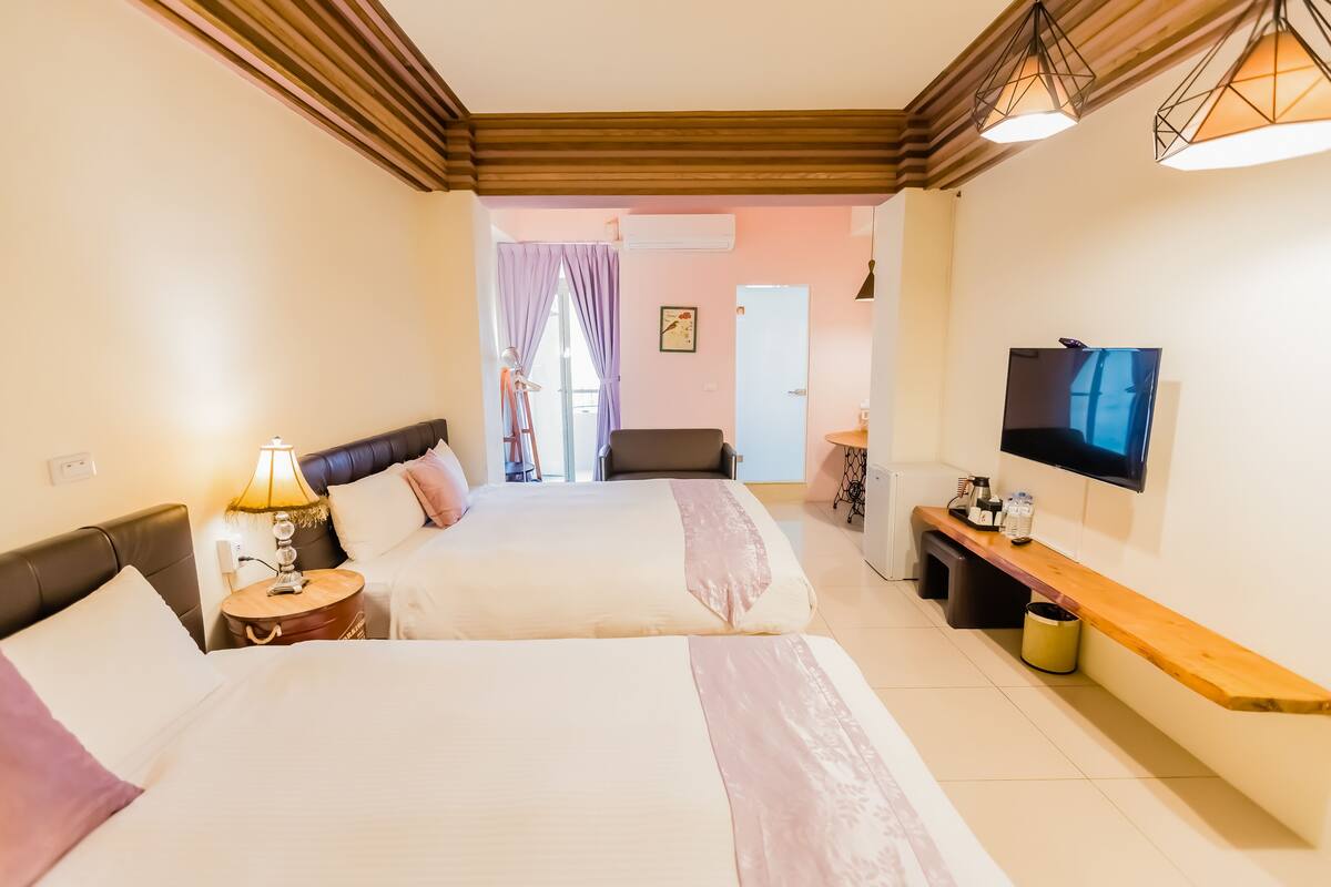 A hotel room with two beds, a TV, a wooden bench, and a desk.