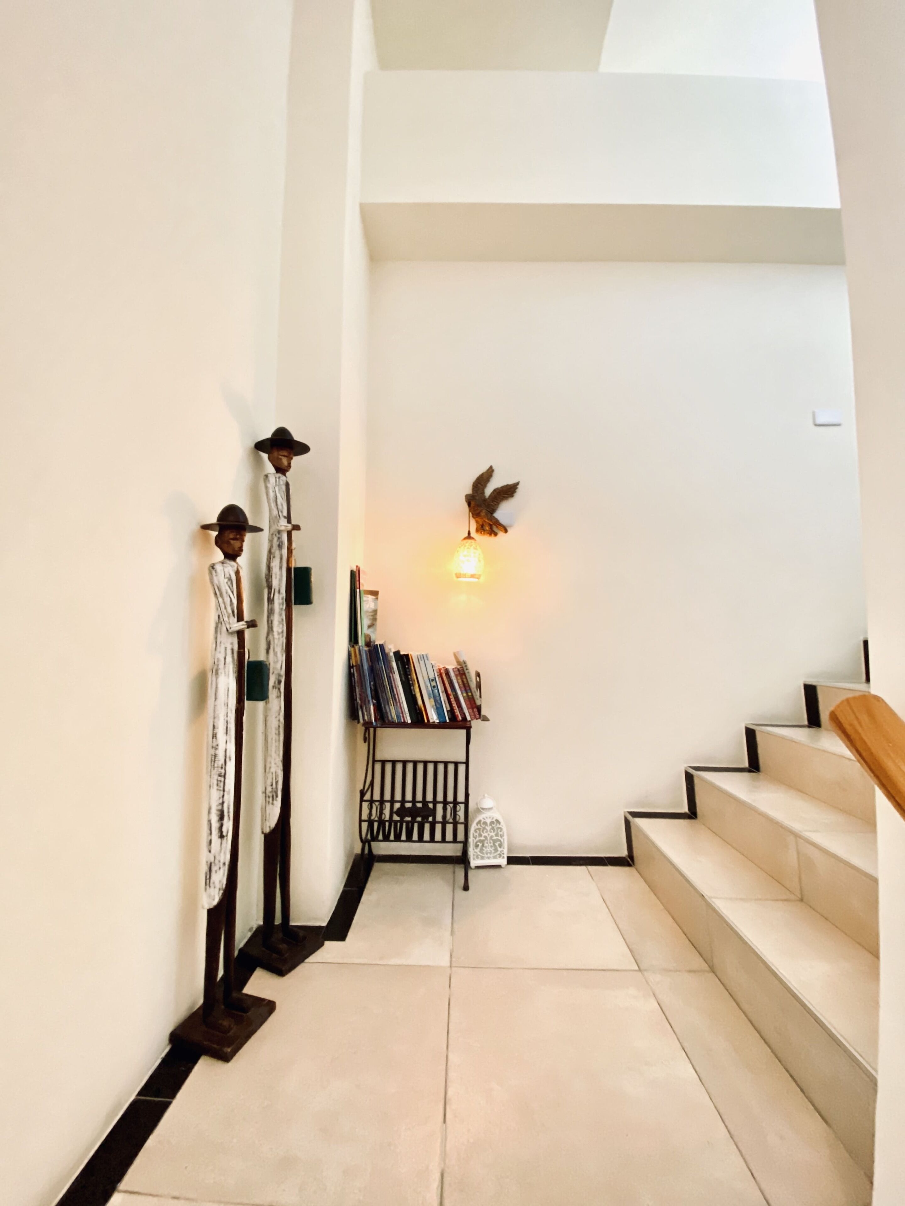 Een trap met een houten leuning, een wandlamp en een klein plankje met boeken en decoratieve objecten.
