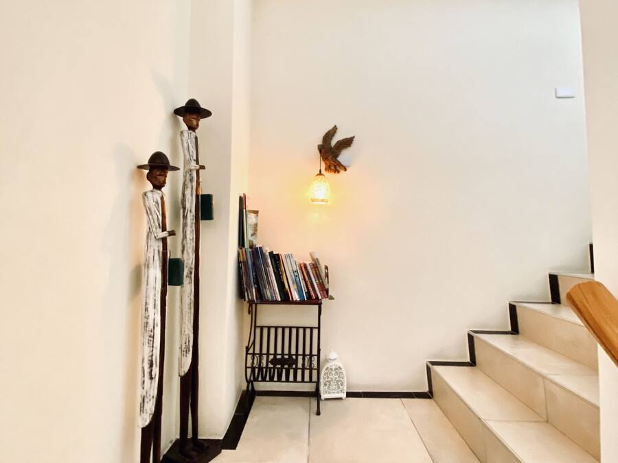 Een trap met een houten leuning, een wandlamp en een klein plankje met boeken en decoratieve objecten.