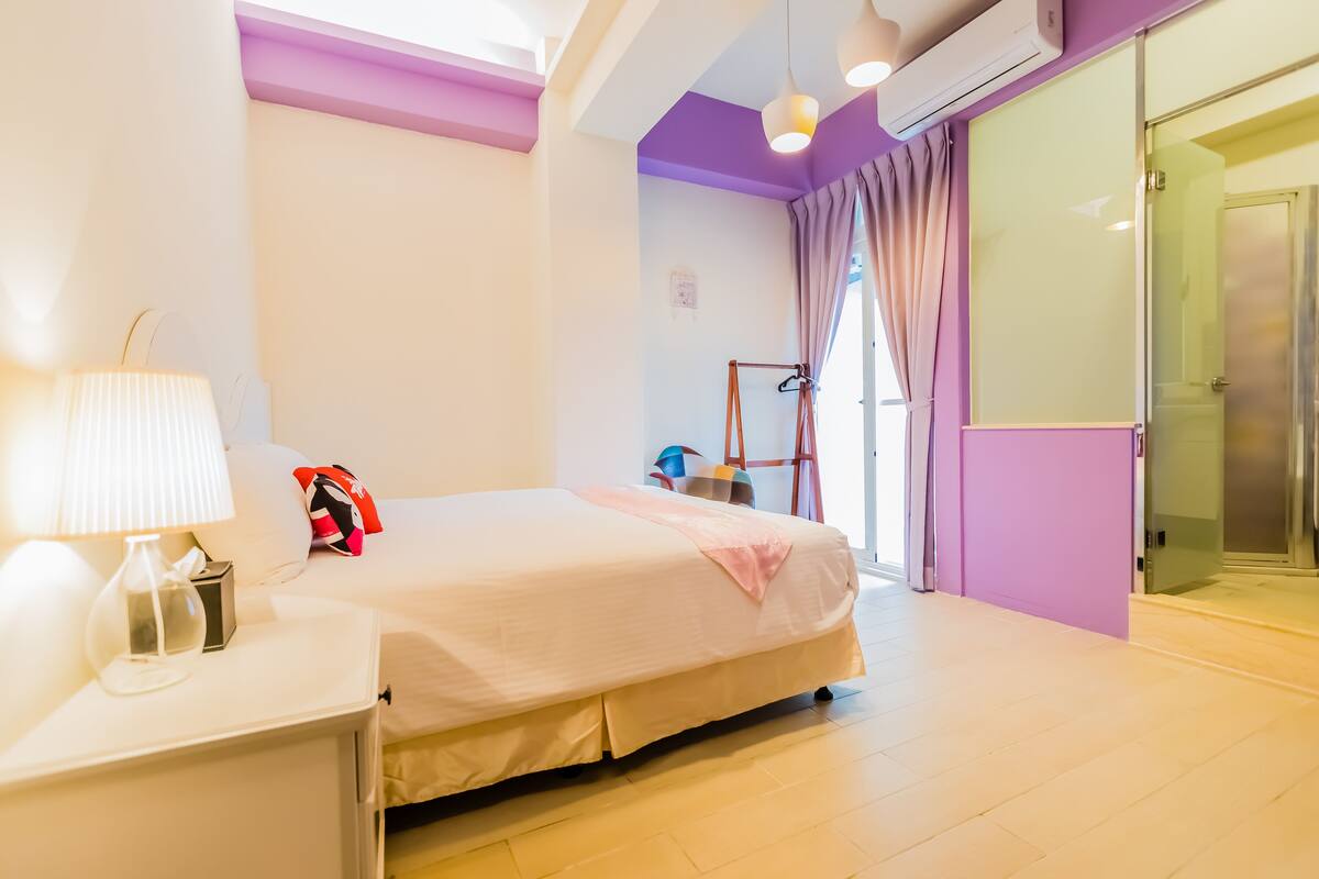 A bedroom with a bed, bedside table, lamp, and a sliding door leading to a bathroom.