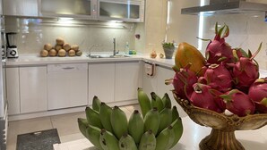 A kitchen with white cabinets, a microwave, a sink, and a fruit bowl containing dragon fruit and bananas. - Tang Villa (Taitung)