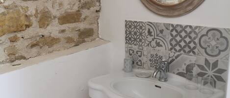 Un baño con pared de piedra, lavamanos blanco y azulejos con diseño.