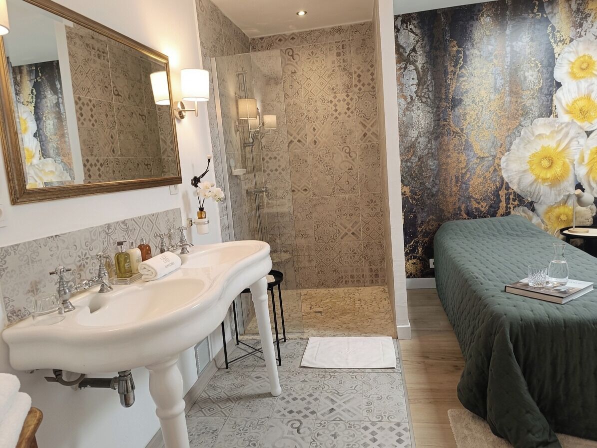Een badkamer met een grote spiegel, wastafel en douche. Er is een bed met een groene dekbedovertrek en een decoratieve wand.