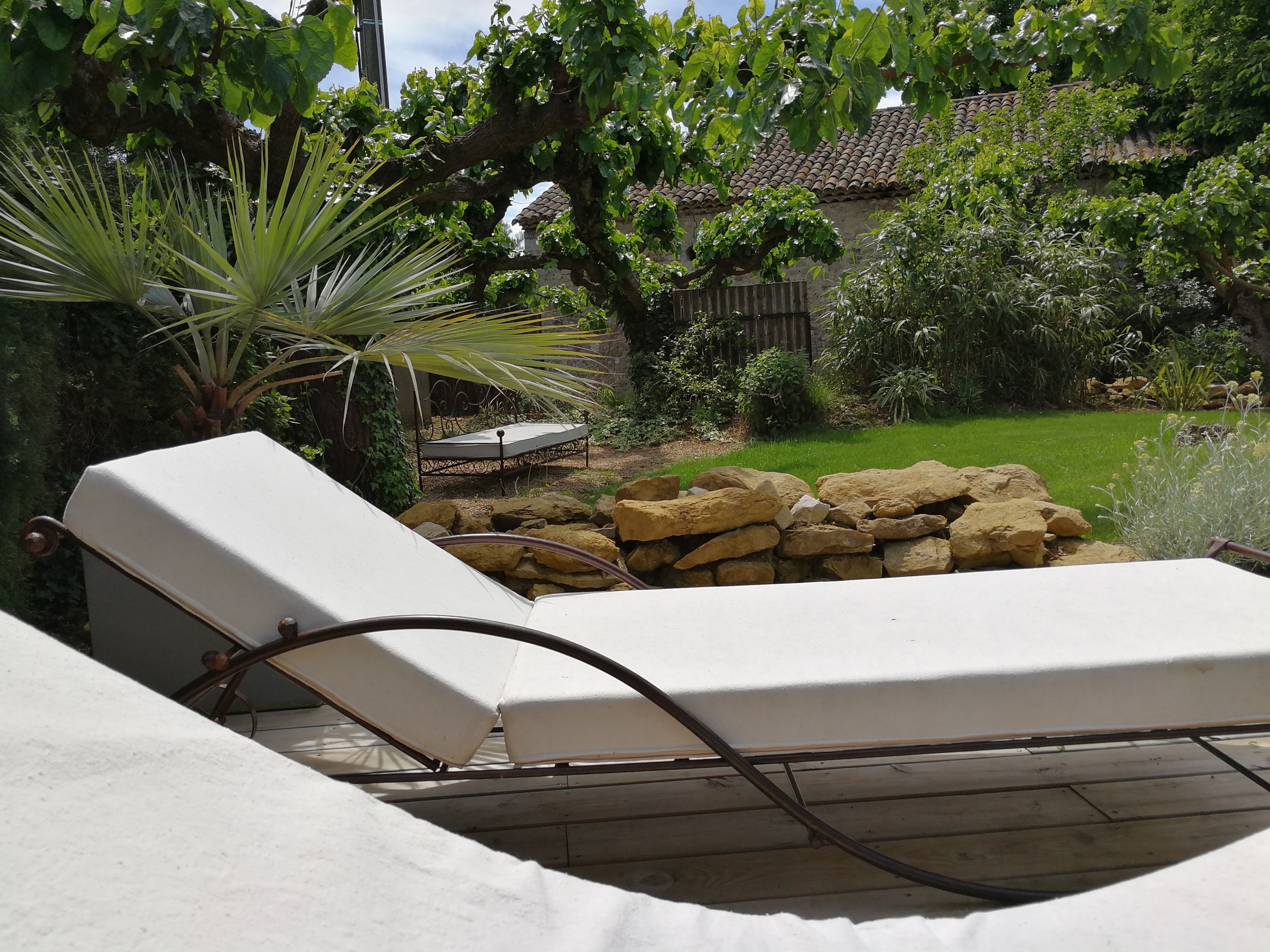 A sunlit outdoor seating area with a stone wall and a bed in the background.