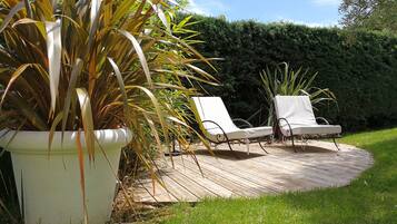 Een houten terras met twee witte ligstoelen en een grote potplant.