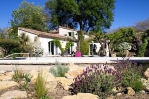 Una villa con tejado de tejas, mobiliario exterior y un jardín con rocas y lavanda.