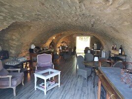 Una habitación subterránea con paredes de piedra, amueblada con sillas, mesas y una estantería para vinos.