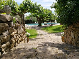 Un sendero de piedra conduce a una zona de piscina rodeada de exuberante vegetación y muros de piedra.