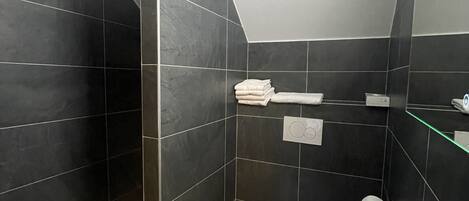A modern bathroom with dark tiles, a white sink, and a mirror.