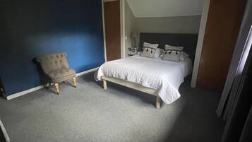 Un dormitorio con cama, una silla y un armario.