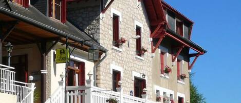 A two-story building with a stone facade, red window frames, and a balcony with white railings.