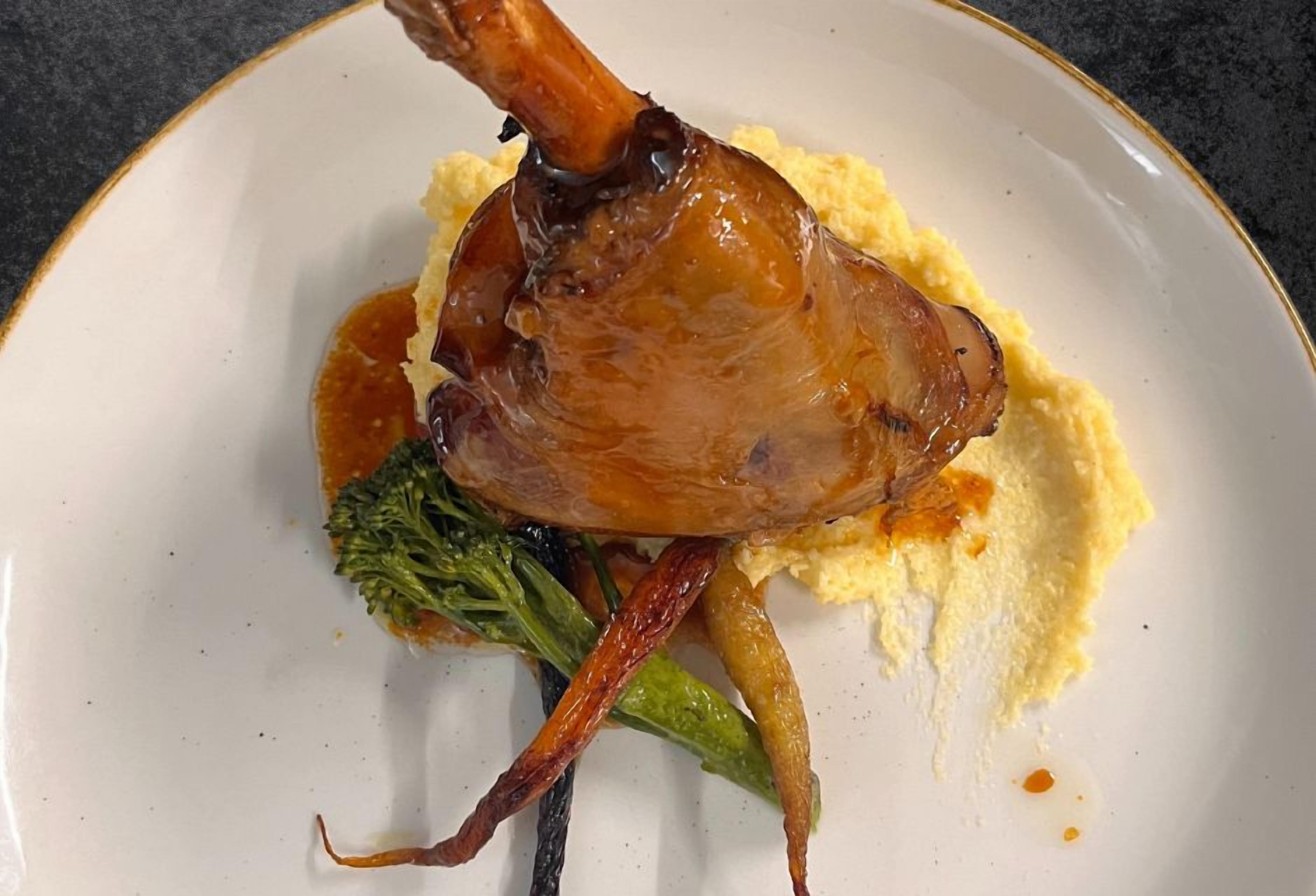 A plate with a roasted duck leg, mashed potatoes, and vegetables.