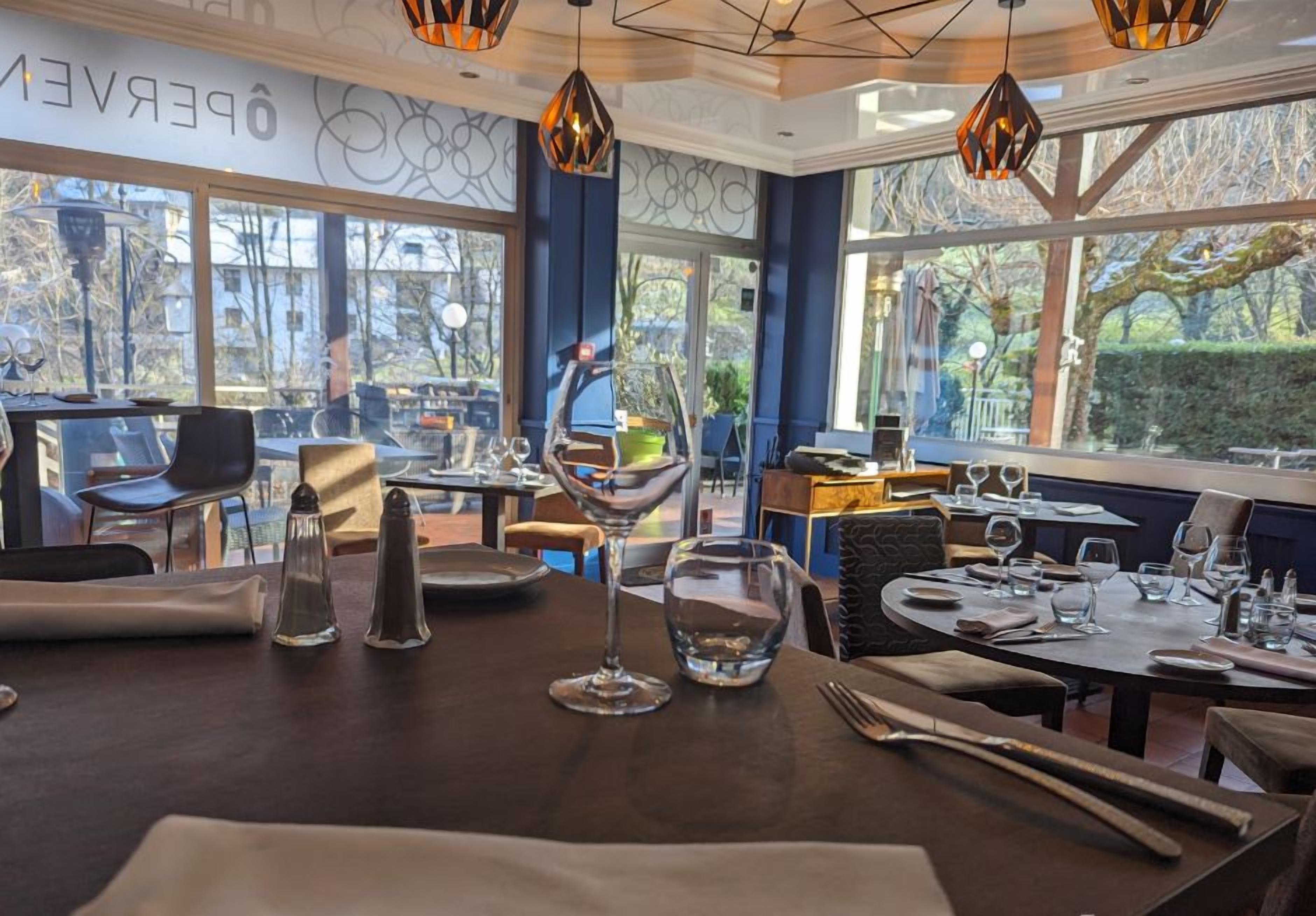 Interior de un restaurante con mesas dispuestas para comer, amplias ventanas que ofrecen vistas al exterior y el logotipo de Logis Hotels.