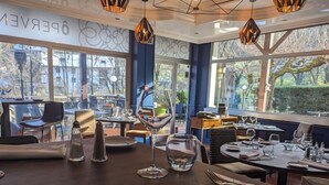 L’intérieur d’un restaurant, avec des tables dressées pour le service, de grandes fenêtres donnant sur l’extérieur et le logo de la chaîne Logis Hotels.
