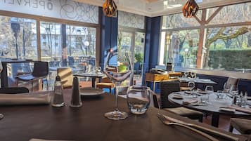 Interior de un restaurante con mesas dispuestas para comer, amplias ventanas que ofrecen vistas al exterior y el logotipo de Logis Hotels.