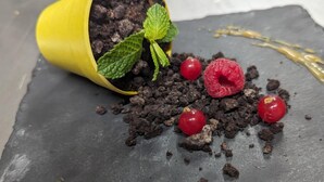Un dessert composé de miettes de chocolat, de framboises et d’une feuille de menthe, le tout présenté sur une ardoise.