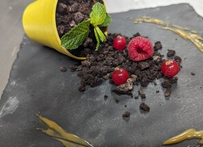 A dessert with chocolate crumbs, raspberries, and a mint leaf on a slate surface. - Hôtel Restaurant Ô Pervenches (Chambery)