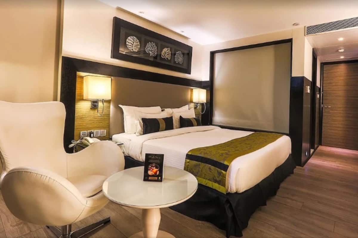A hotel room with a large bed, a chair, a small table, and a wall-mounted artwork.