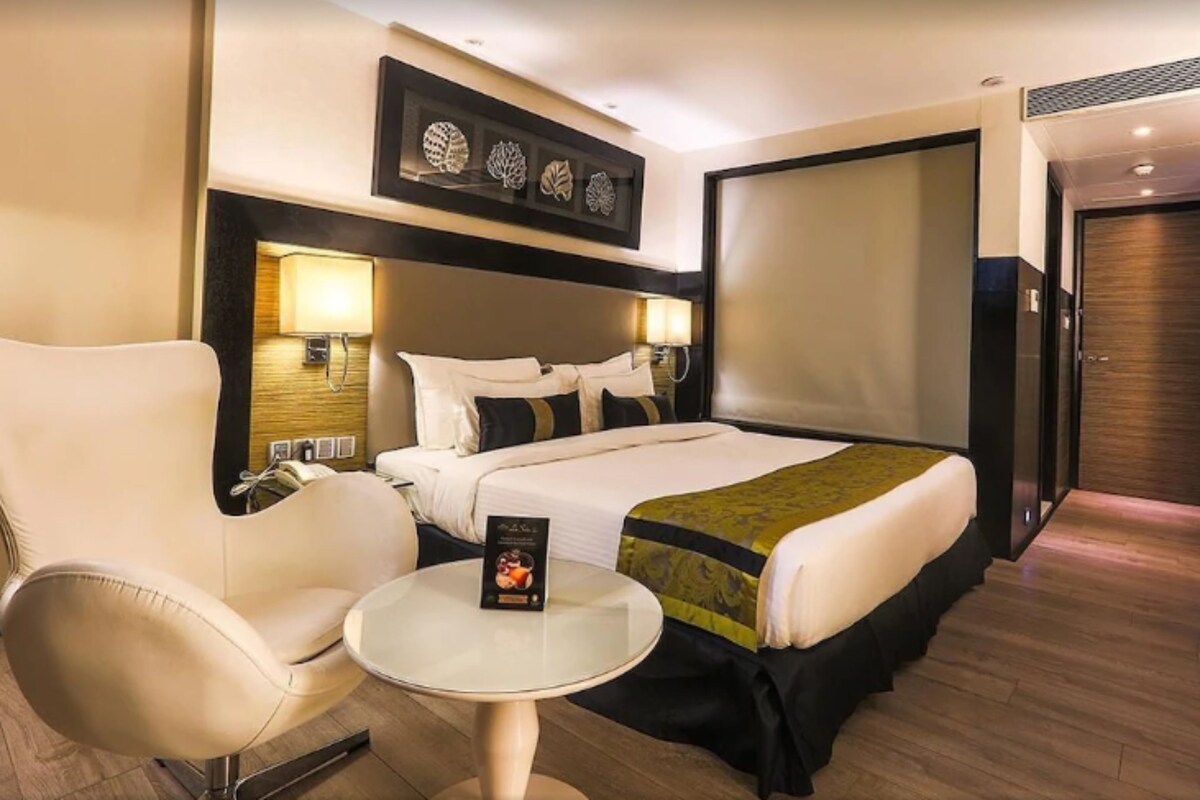 Una habitación de hotel con una cama, una silla, una mesita y una lámpara de pared.