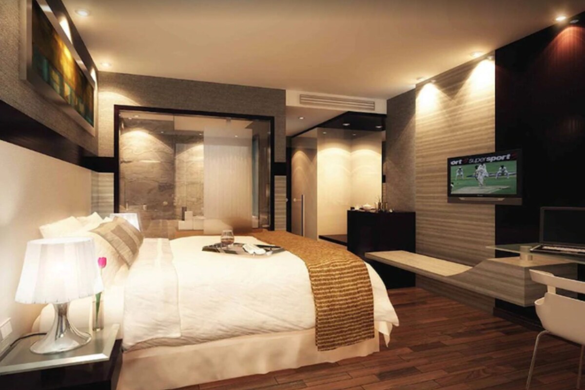 Una habitación de hotel moderna con una cama grande, mesita de noche, lámpara, televisor y un banco.