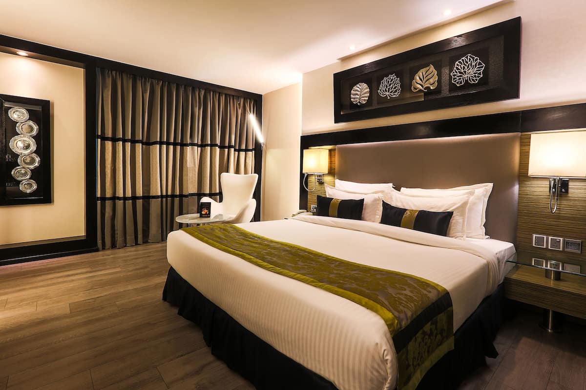 A hotel room with a large bed, a chair, a nightstand, and a wall with decorative leaf art.