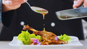 En kok hælder sauce over en stegt and på en tallerken med grønt og blomster.