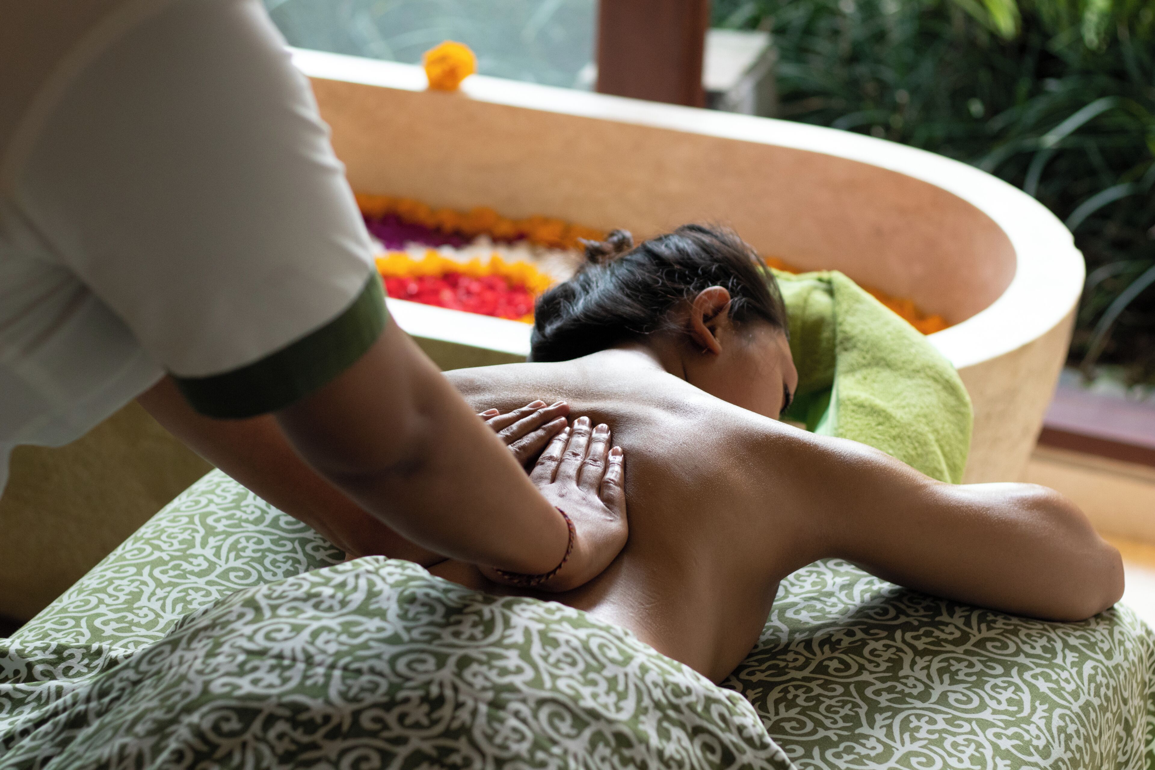 En person modtager massage i et rum med et blomsterfyldt badekar.