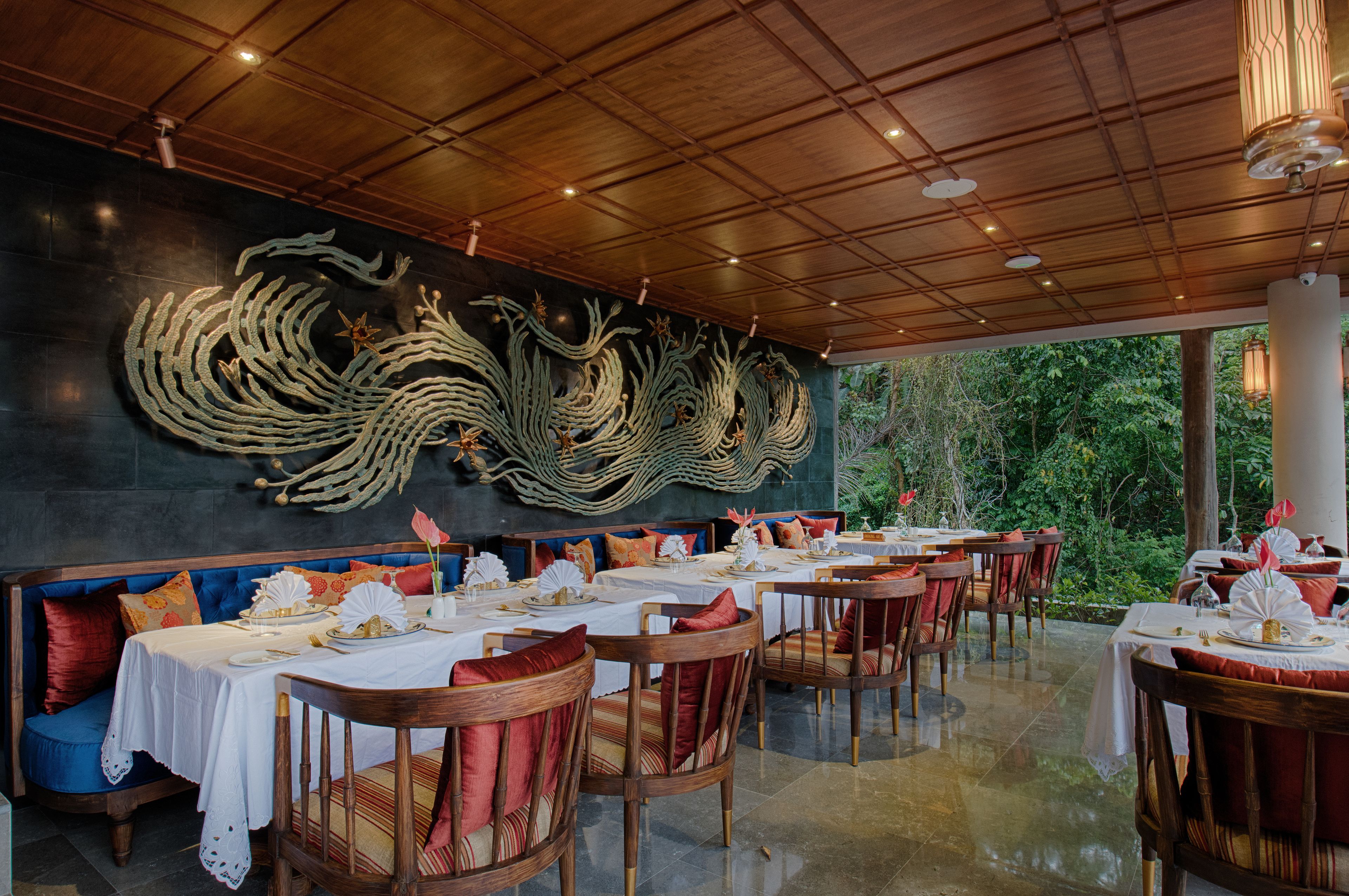 A restaurant with a traditional Asian dragon mural on the wall, wooden tables with white tablecloths, and red cushioned chairs.