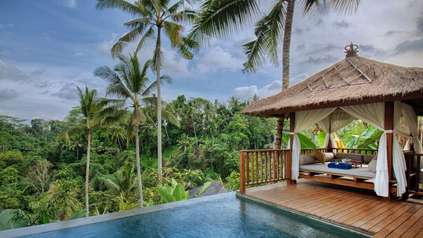 Une piscine avec une terrasse en bois et un gazebo à toit de chaume.